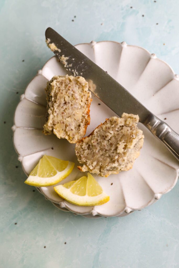 Lemon Cashew Chia Seed Muffin split in half with a knife on two places with two lemon wedges by Flora & Vino
