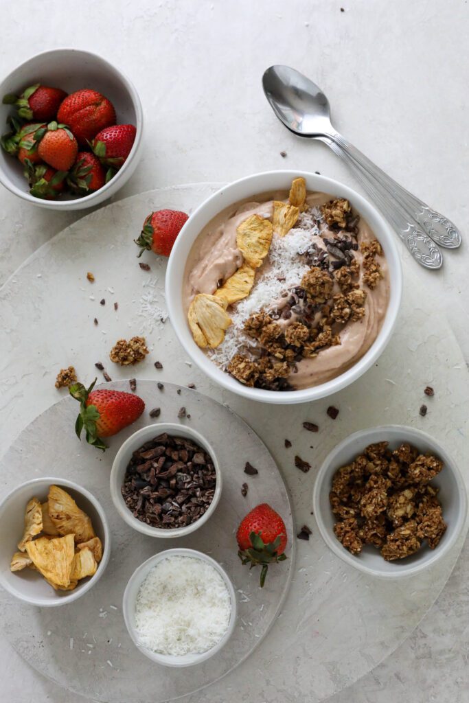 Strawberry Mango Smoothie Bowl served in bowl topped with dried pineapple, shredded coconut, and granola with fresh strawberries on the side
