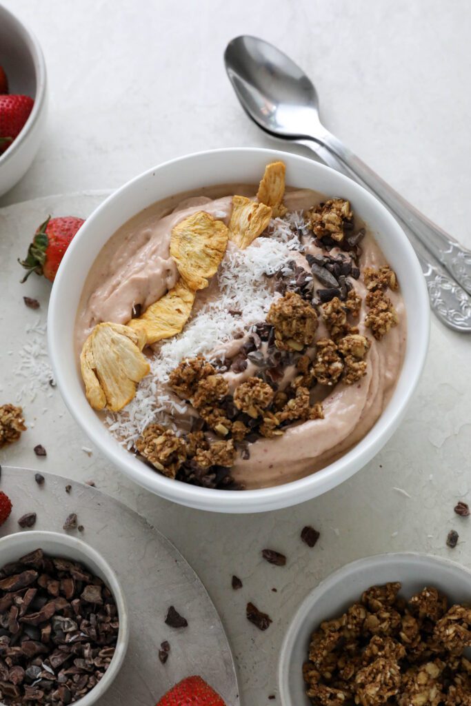Strawberry Mango Smoothie Bowl served in bowl topped with dried pineapple, shredded coconut, and granola with fresh strawberries on the side