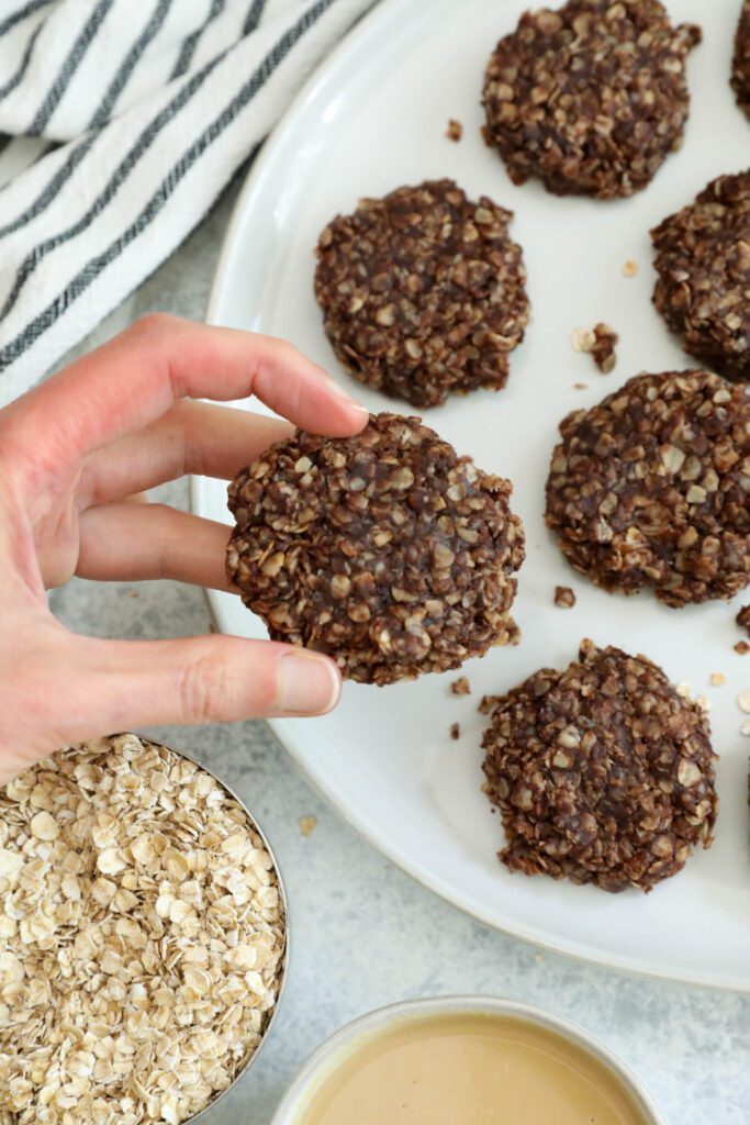 hand lifting Chocolate Tahini No-Bake Cookie off of plate by Flora & Vino