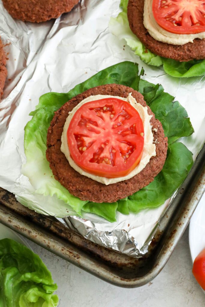 Smoky White Bean & Beet Burgers served on lettuce leaves with hummus and tomato on aluminum lines baking sheet with