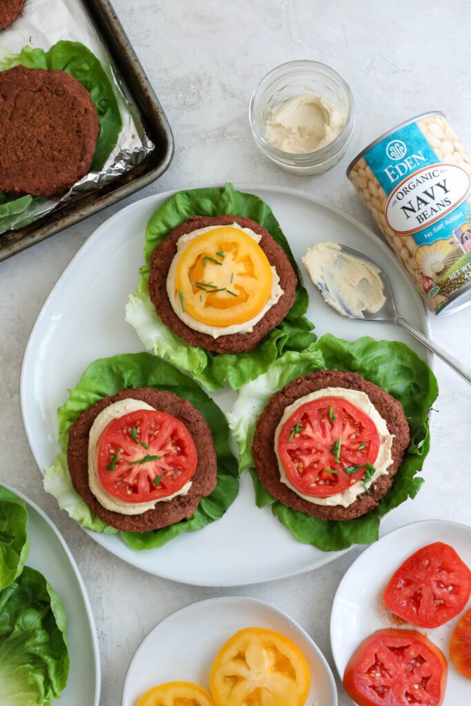 Smoky White Bean & Beet Burgers served on lettuce leaves on white plate topped with hummus and tomato 