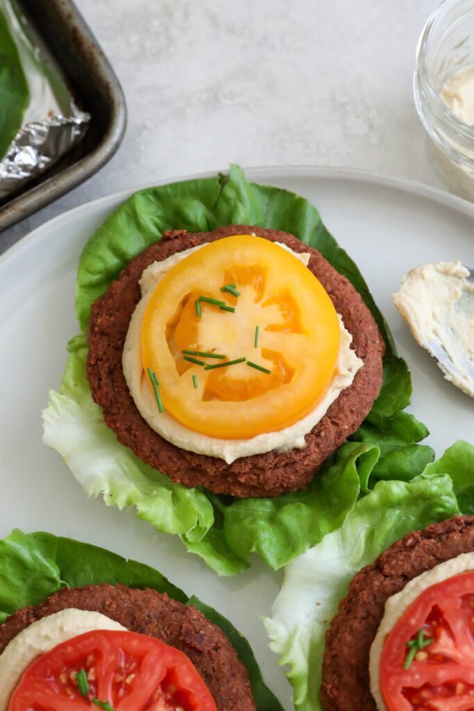 Smoky White Bean & Beet Burgers served on lettuce leaves on white plate topped with hummus and tomato 