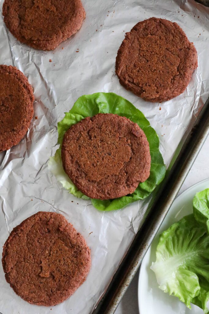 Smoky White Bean & Beet Burgers baked on aluminum lined baking sheet with one burger on a lettuce leaf