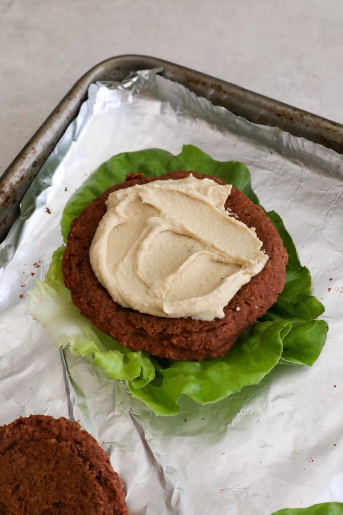 Smoky White Bean & Beet Burger on lettuce leaf topped with hummus