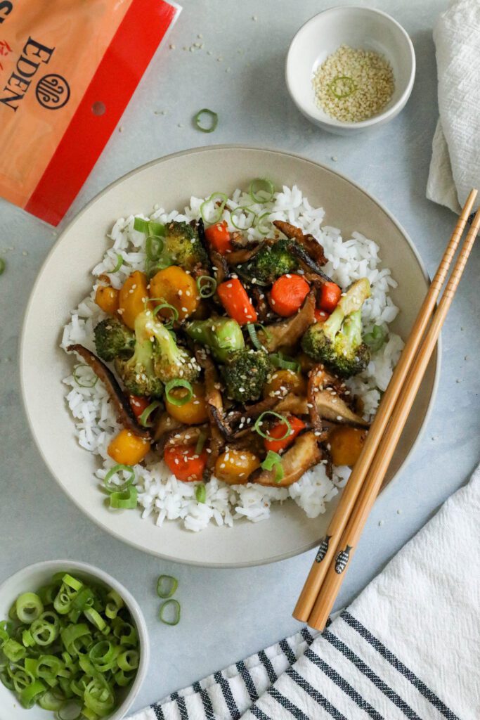 Sesame Shiitake & Broccoli Stir-Fry served over jasmine rice with green onion and sesame seeds on top and chopsticks on the side by Flora & Vino