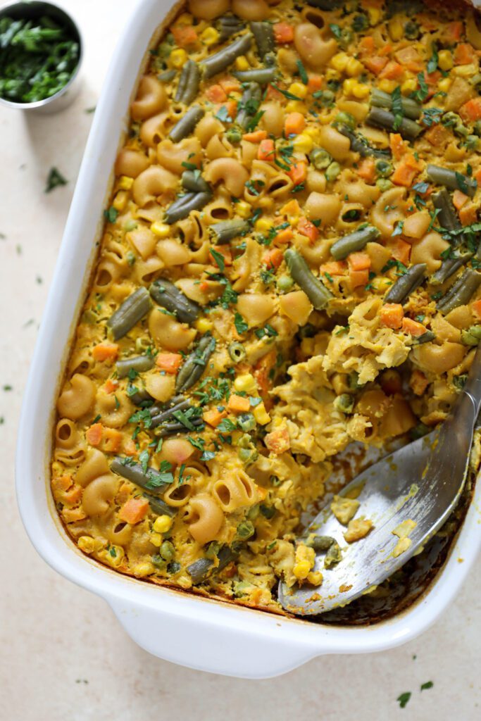 Chickpea Macaroni Casserole in casserole dish with serving spoon and parsley by Flora & Vino