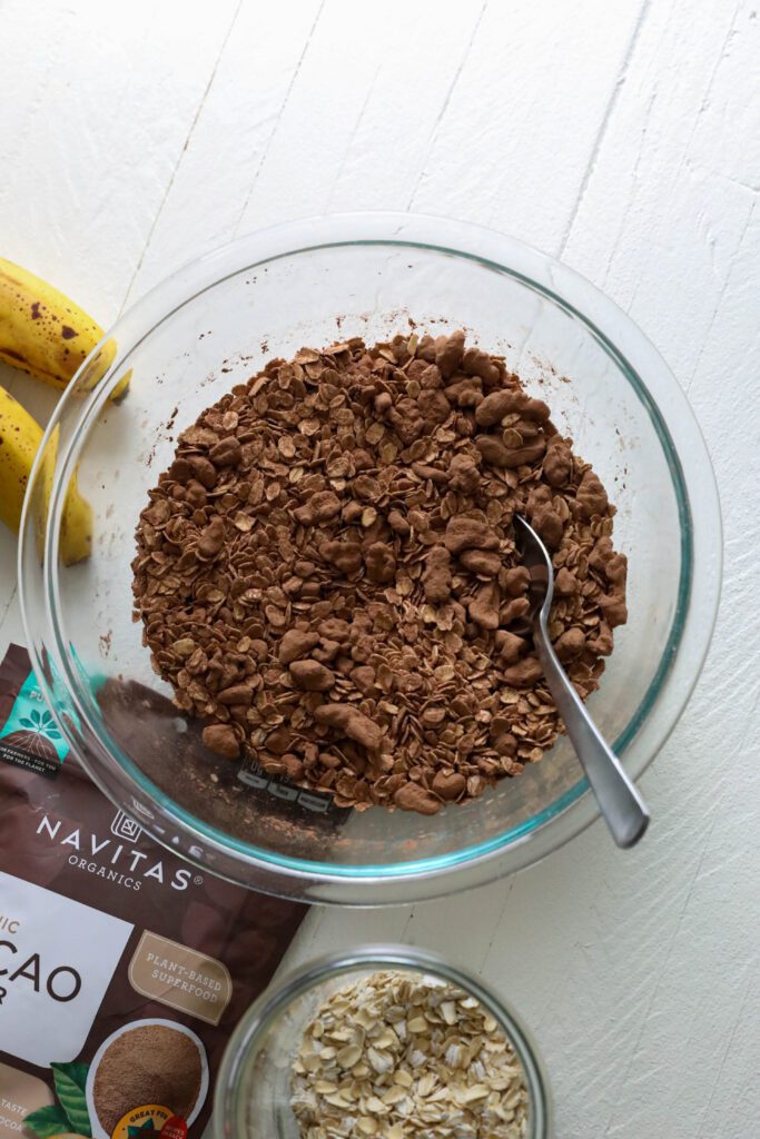 oats and cacao powder in large bowl with a spoon by Flora & Vino 
