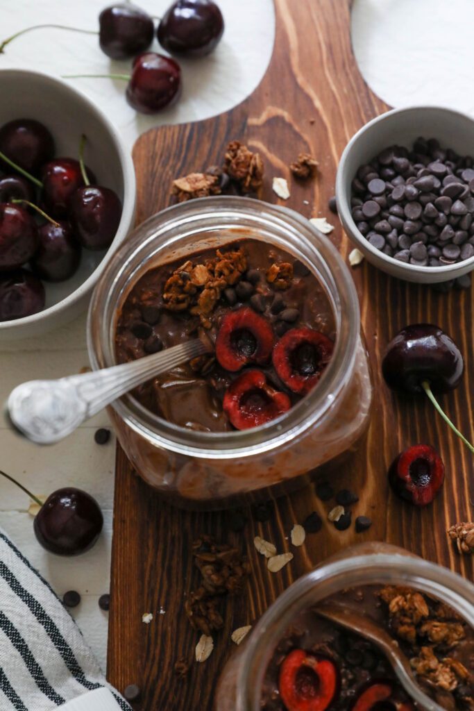 Chocolate Cherry Overnight Oats served in mason jars with spoons topped with cherries and chocolate chips 