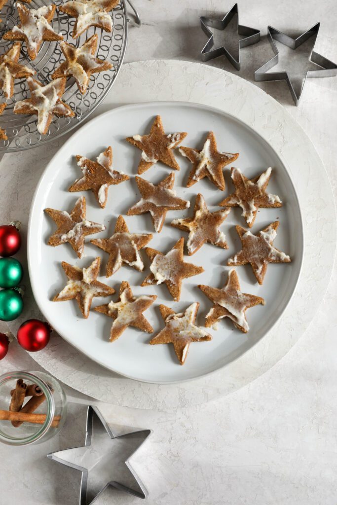 Cinnamon SunButter Star Cookies (Zimtsterne) served on a plate surrounded by ornaments by Flora & Vino