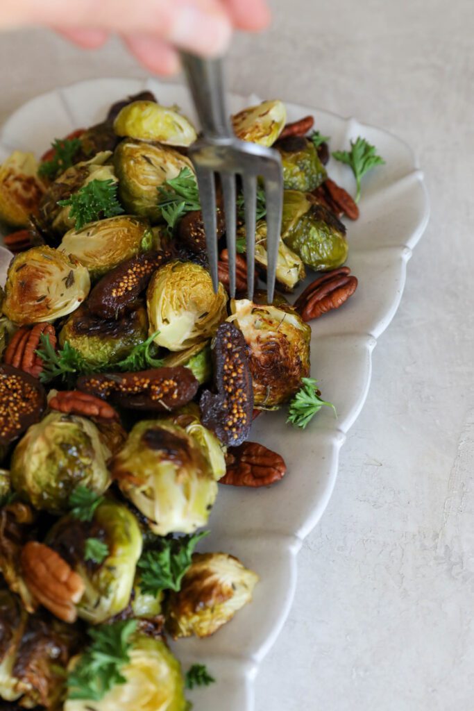 fork stabbing Roasted Brussels Sprouts with Figs & Pecans by Flora & Vino