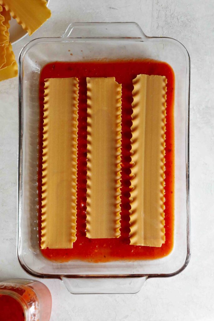 marinara sauce with lasagna noodles on top in casserole dish by Flora & Vino