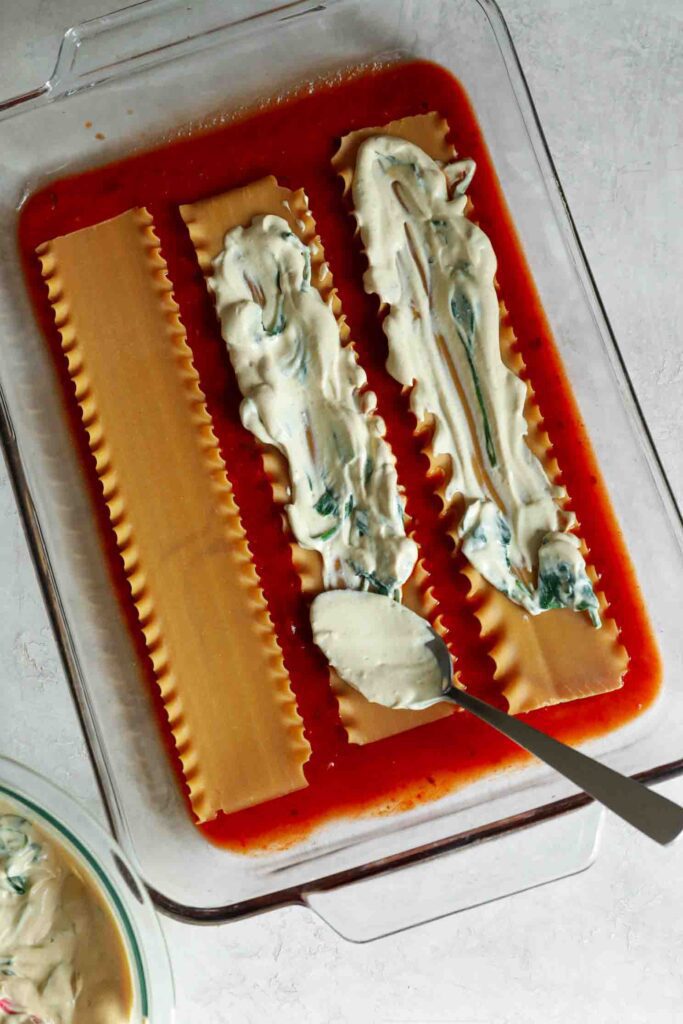 marinara sauce with lasagna noodles topped with cashew ricotta in casserole dish by Flora & Vino
