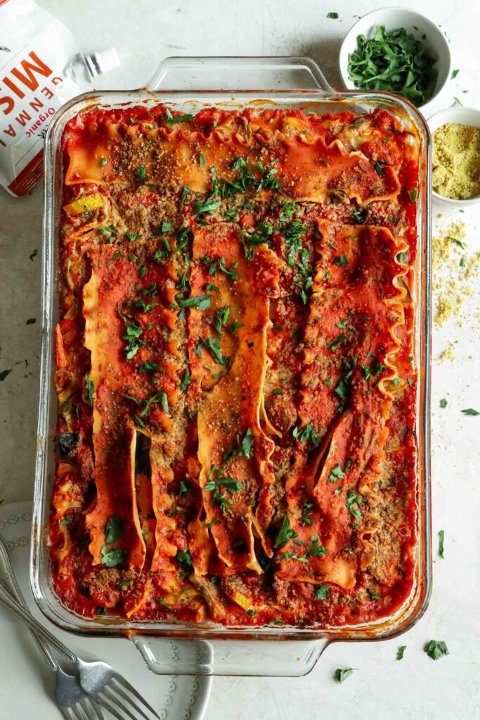 Vegan Vegetable Lasagna with Tofu Ricotta baked in casserole dish and topped with parsley and vegan parmesan by Flora & Vino