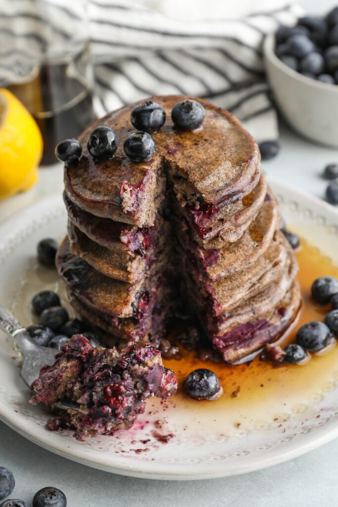 Blueberry Buckwheat Pancakes stacked with a bite missing by Flora & Vino