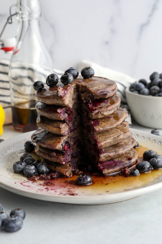 Blueberry Buckwheat Pancakes stacked on a plate with bite missing by Flora & Vino