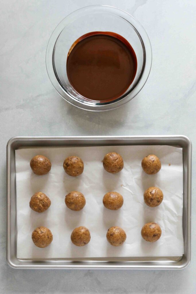 Cookie Dough Protein Truffles rolled onto parchment lined baking sheet with melted chocolate by Flora & Vino