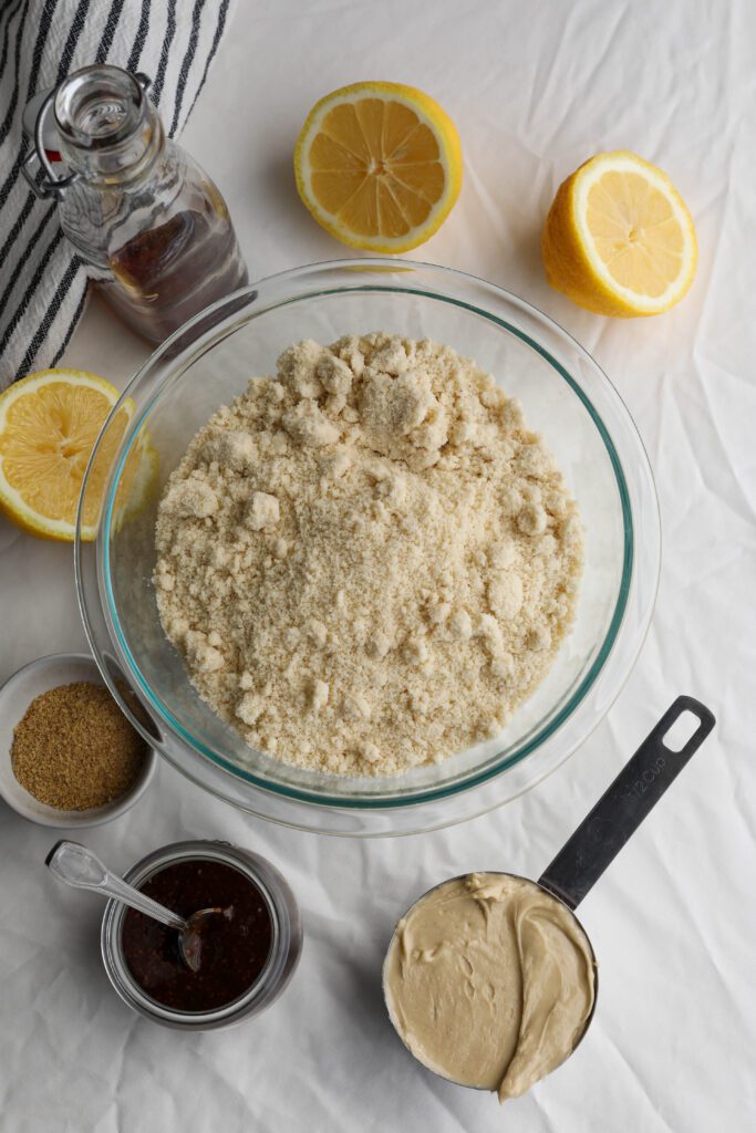 almond flour, halved lemons, cashew butter, maple syrup, coconut sugar, and jam on white and blue striped towel