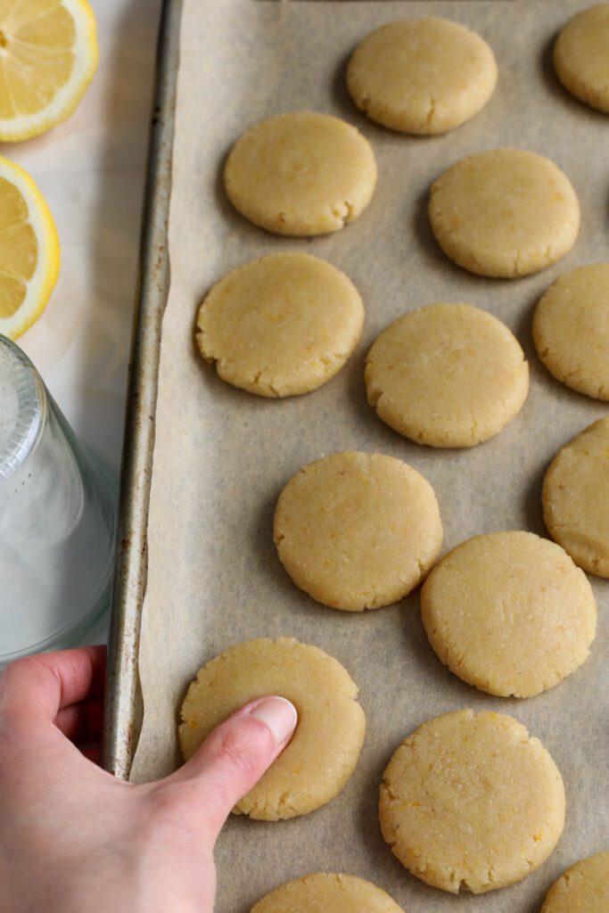 hand placing thumbprint in Lemon Almond Flour Thumbprint Cookies on parchment lined baking sheet