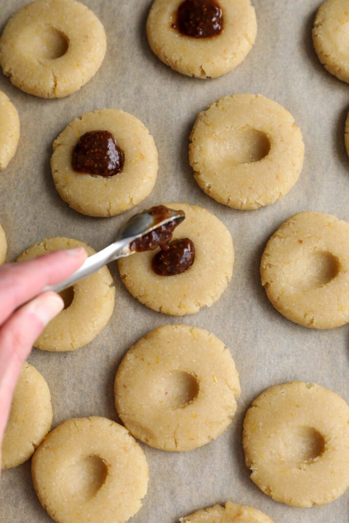 hand adding jam to center on almond flour cookies