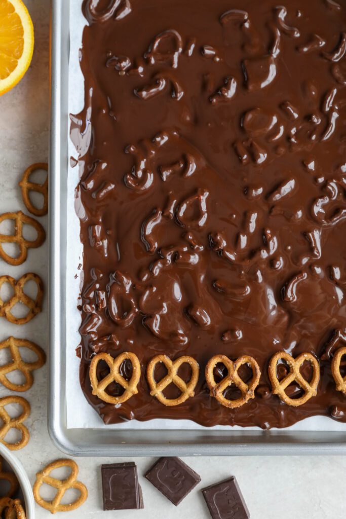 adding pretzels in a row on melted chocolate pretzel bark by Flora & Vino