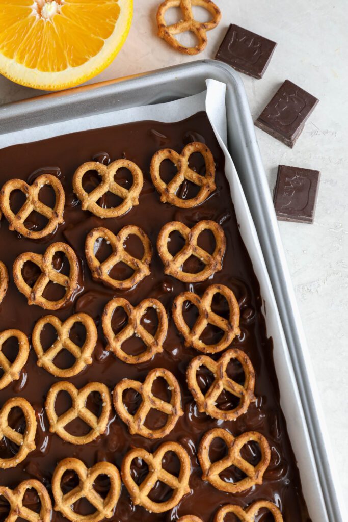 Orange Chocolate Pretzel Bark process photos on parchment lined baking sheet with chocolate squares and pretzel and orange on side by Flora & Vino