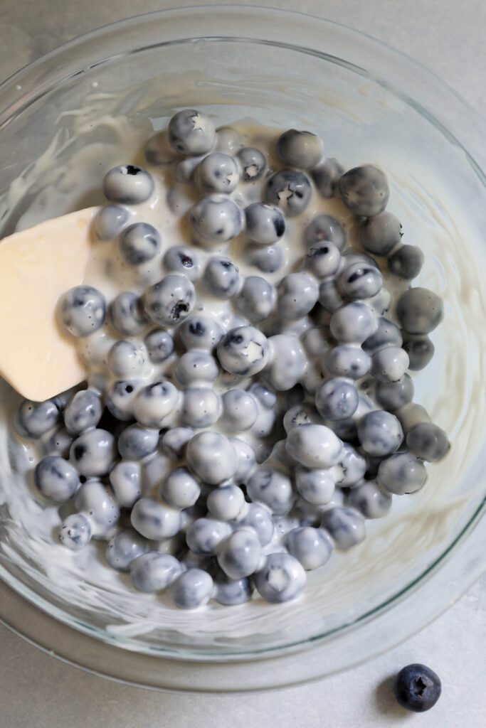 blueberries coated in yogurt in bowl with spatula 