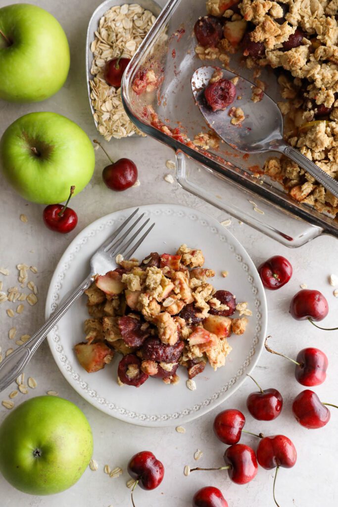 Apple cherry tahini crumble served on plate surrounded by cherries and apple 