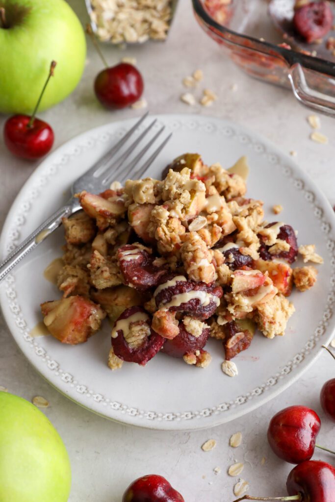 Apple cherry tahini crumble served on plate surrounded by cherries and apple 
