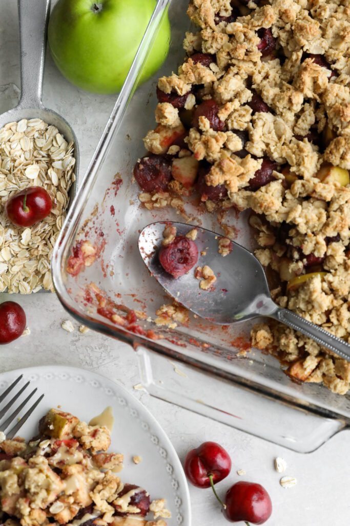 Apple Cherry Tahini Crumble served in glass baking dish with spoon and oats 