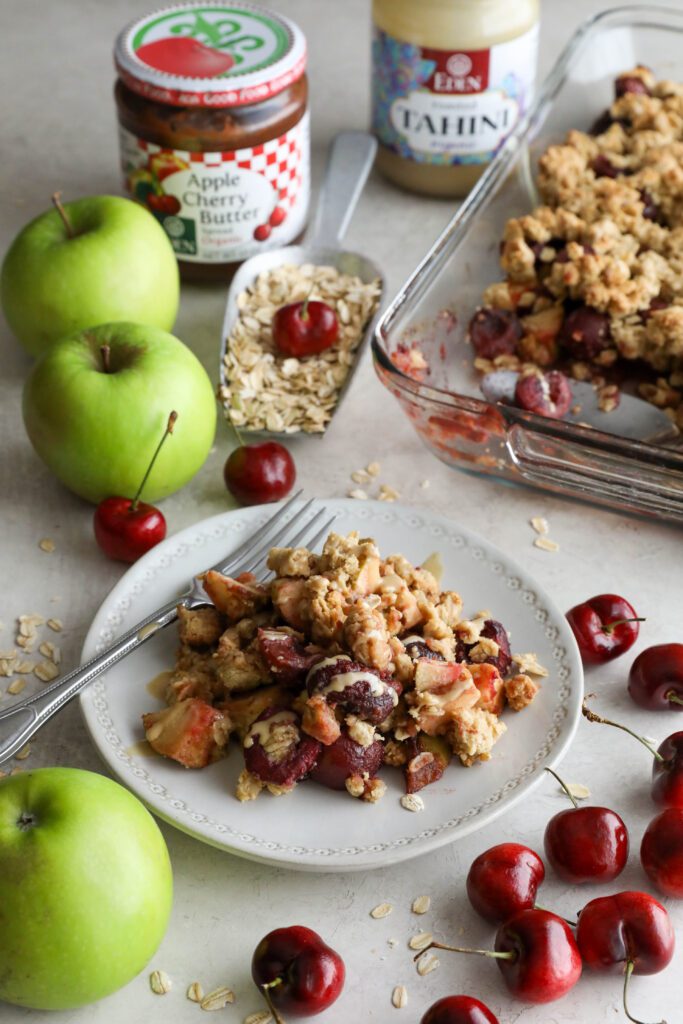 Apple cherry tahini crumble served on plate surrounded by cherries and apple 