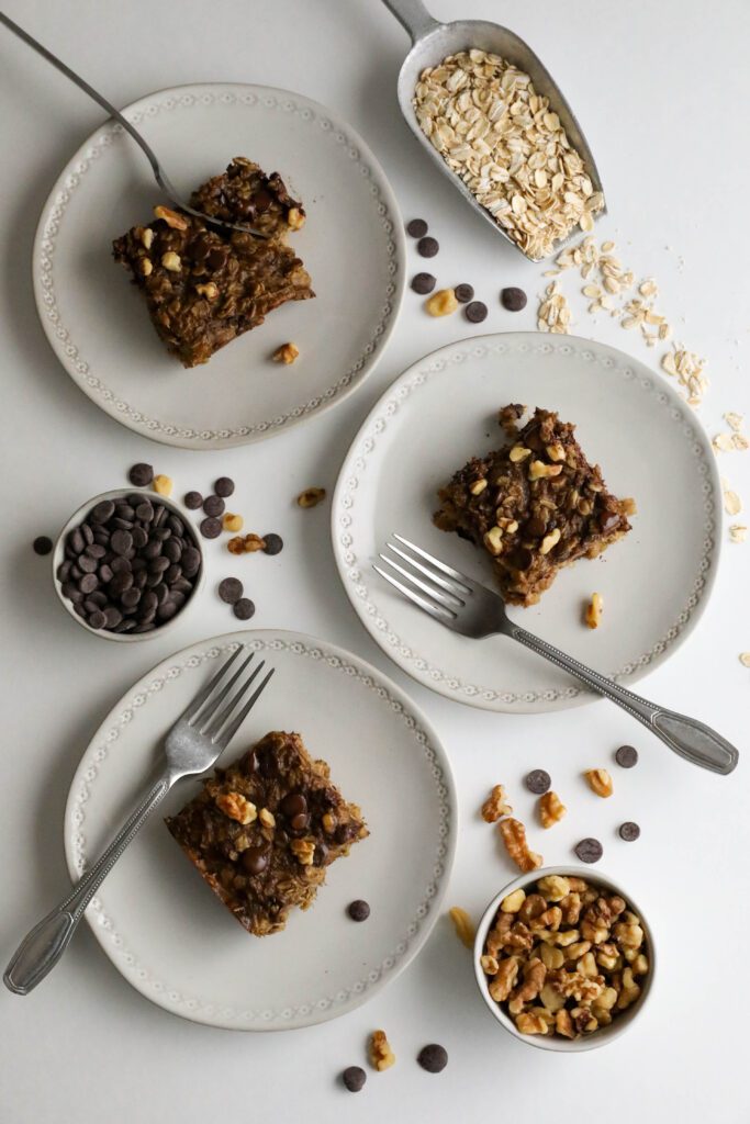 Banana Oatmeal Chocolate Chip Breakfast Bars served on plates with two forks with oatmeal, chocolate chips, and walnuts scattered