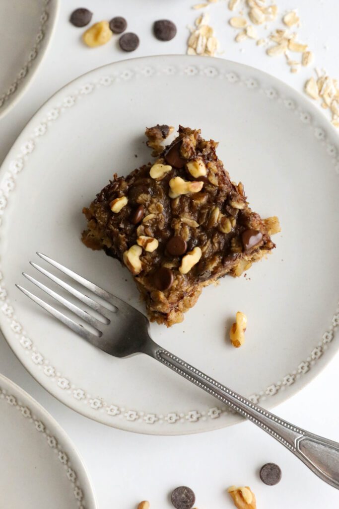Banana Oatmeal Chocolate Chip Breakfast Bars served on plates with two forks with oatmeal, chocolate chips, and walnuts scattered