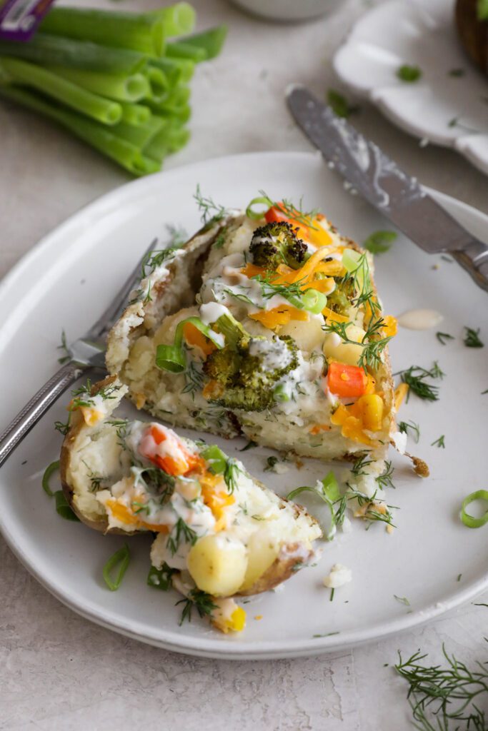 Veggie Loaded Twice Baked Potato cut open on a plate topped with fresh dill and green onion and fork and knife