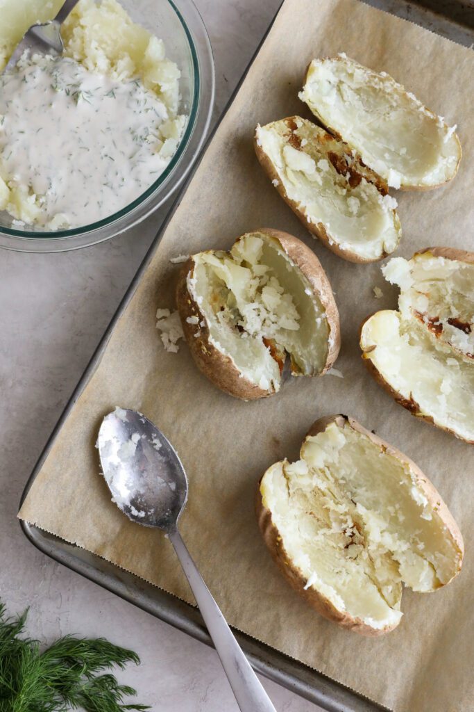 russet potatoes baked on parchment lined baking sheet and split in half with some removed 