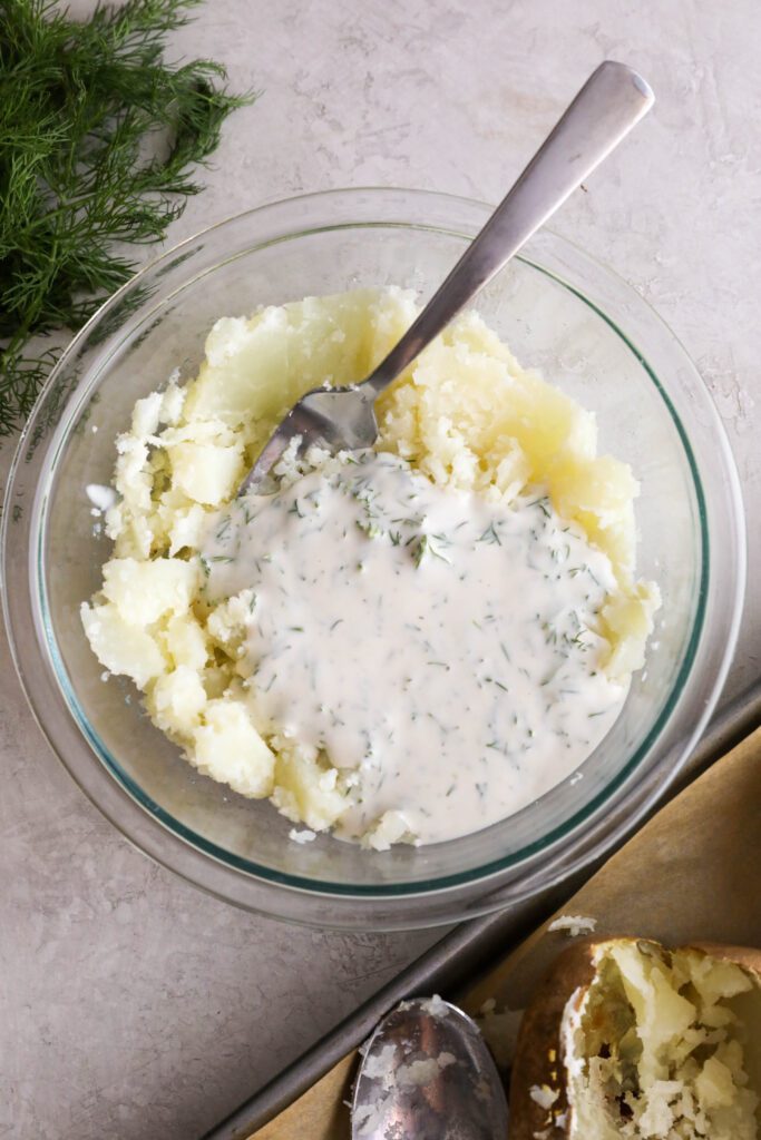 smashed potatoes in bowl topped with yogurt dill sauce in bowl with fork