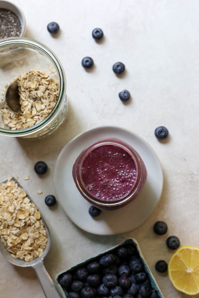 blueberry milk in mason jar with oats in jar and scattered blueberries by Flora & Vino