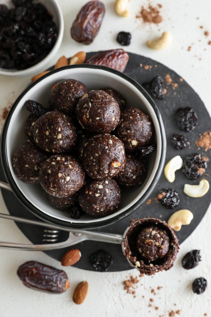 Grain-Free Chocolate Cherry Bliss Balls served in a bowl surrounded by cashews, dried cherries, and Medjool dates by Flora & Vino