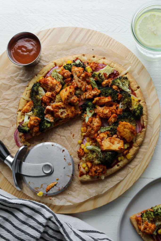 BBQ Tofu Pizza on serving board with pizza cutter by Flora & Vino