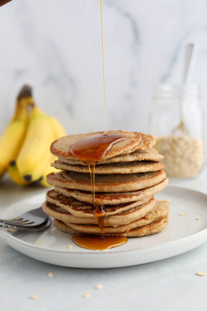 Protein Oat Blender Pancakes stacked on a plate with maple syrup poured by Flora & Vino 