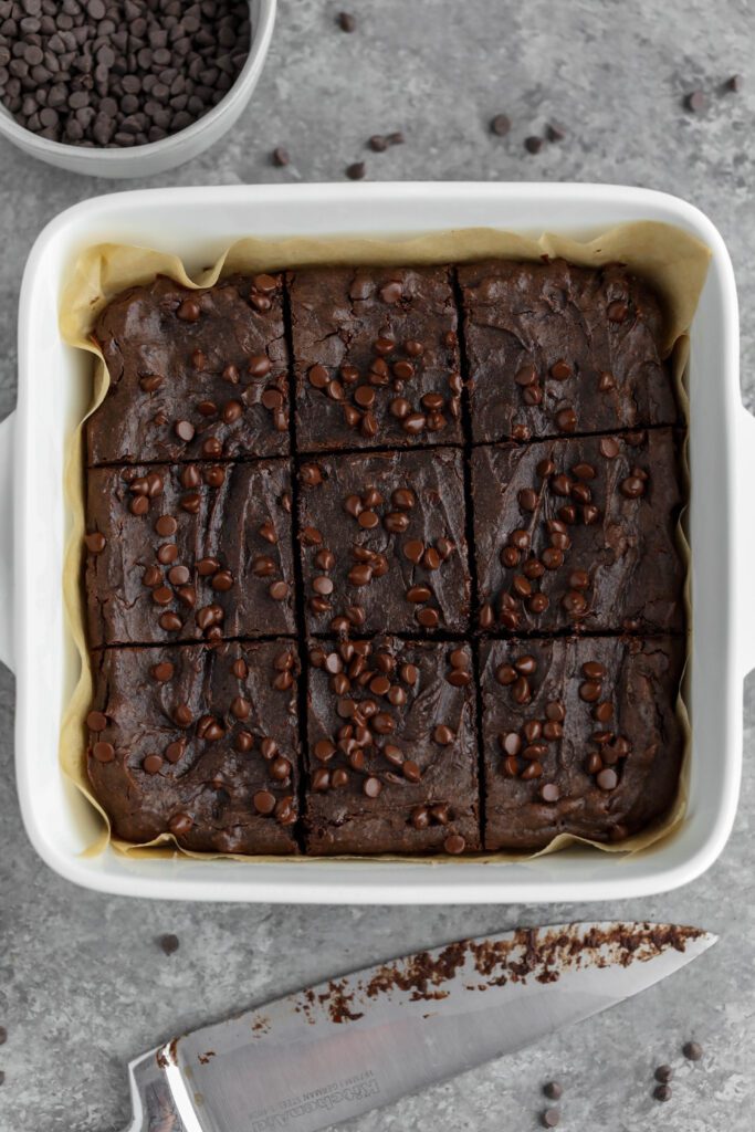 Flourless Vegan Brownies sliced in pan with knife and chocolate chips by Flora & Vino 