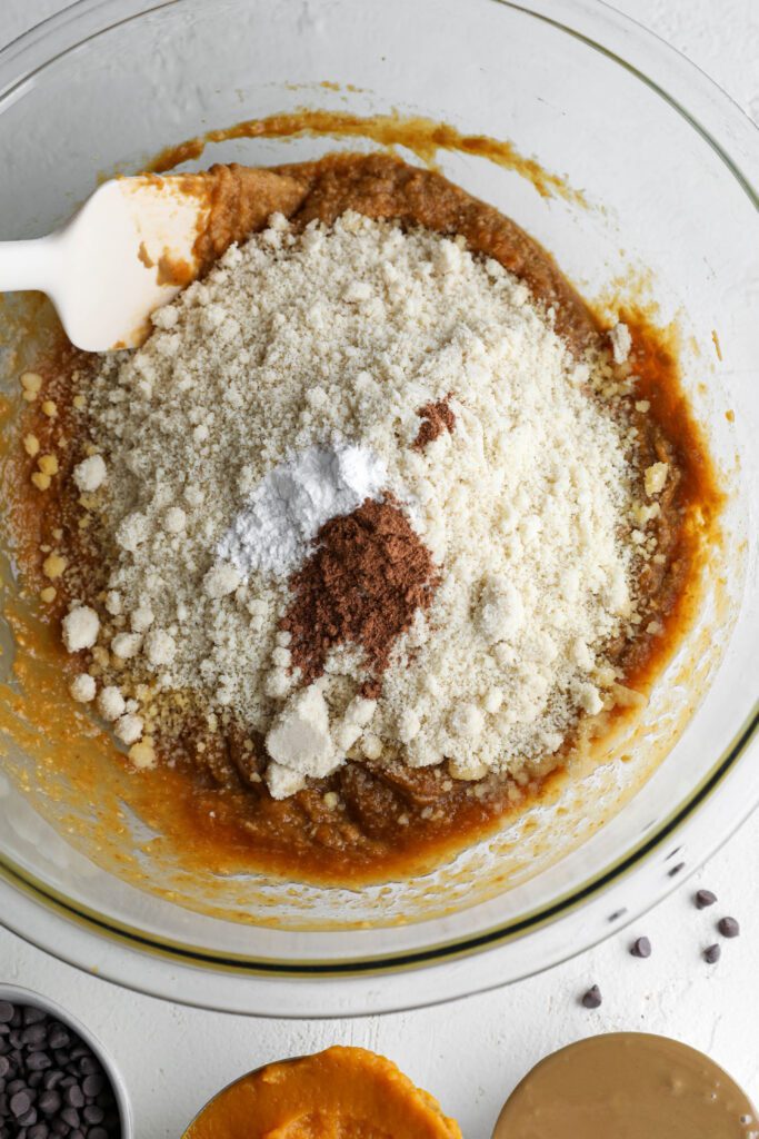 mixing pumpkin muffin batter in a bowl with a spatula by Flora & Vino