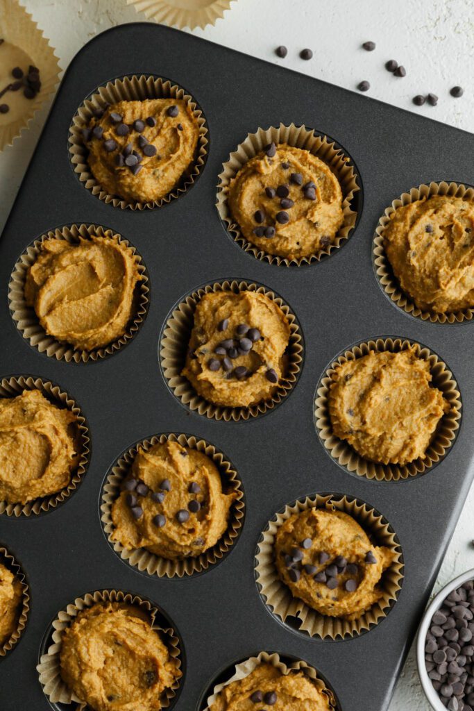 pumpkin muffins in parchment lined muffin tin with chocolate chips on top by Flora & Vino