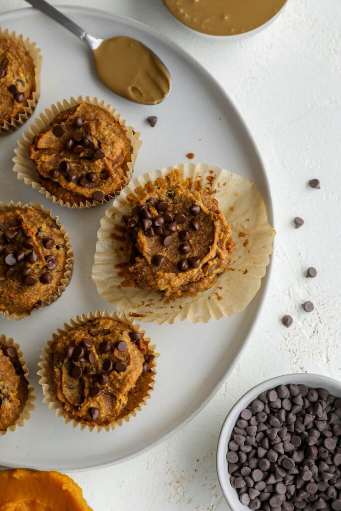 Pumpkin SunButter Chocolate Chip Muffins on plate with chocolate chips scattered by Flora & Vino