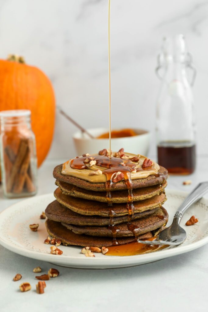 Vegan Pumpkin Buckwheat Pancakes stacked on plate with maple syrup drizzled 