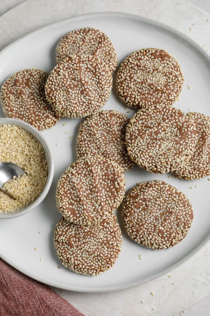 Chocolate Sesame Tahini Cookies on plate with bowl of sesame seeds by Flora & Vino