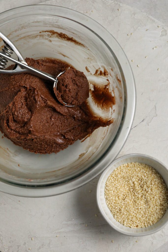 Chocolate Sesame Tahini Cookie batter with cookie scoop in glass bowl by Flora & Vino