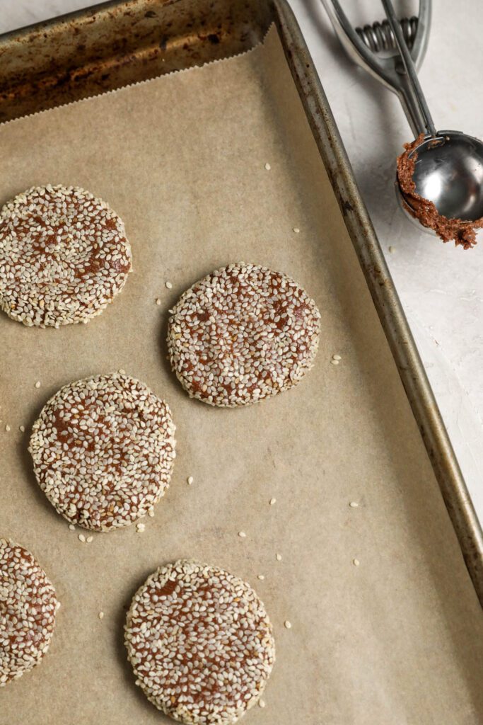 Chocolate Sesame Tahini Cookies rolled in sesame seeds and flattened on parchment lined baking sheet by Flora & Vino 