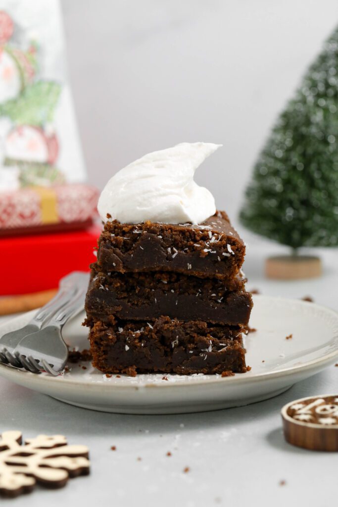 SunButter Gingerbread Bars stacked on a plate with coconut whipped cream by Flora & Vino
