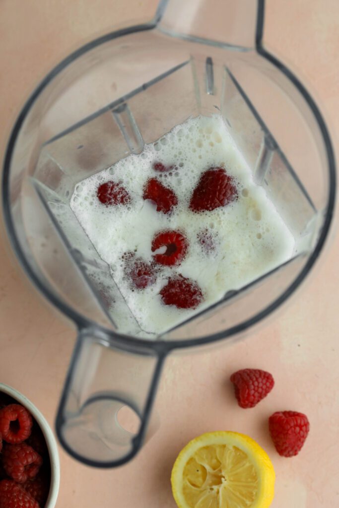 raspberries, almond milk, maple syrup, and lemon juice in a blender with raspberries and lemon on the side by Flora & Vino